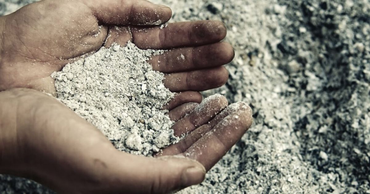 Hands holding a pile of ash with more ash scattered in the background.